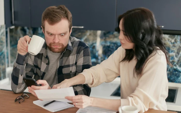 Shocked Man Holding Coffee Mug looking at utility bill with partner